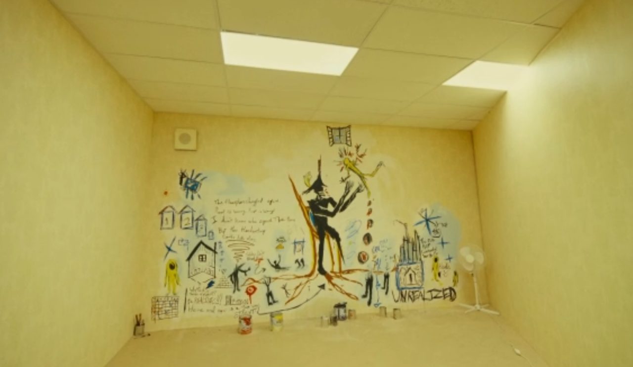 A mural on a yellow-room wall: a black figure, scrawled text, a city
